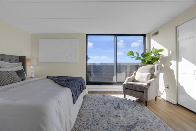 bedroom featuring a wall of windows and light hardwood / wood-style flooring