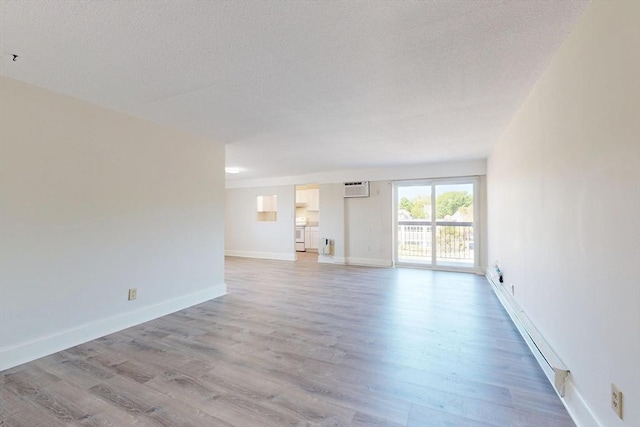47 Mystic St Unit 4E, Arlington, MA 02474 - unfurnished living room featuring a baseboard heating unit, light wood-style flooring, a wall mounted AC, a textured ceiling, and baseboards
