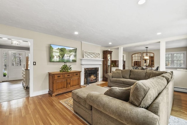 living area featuring recessed lighting, a fireplace with flush hearth, a baseboard heating unit, baseboards, and light wood-style flooring