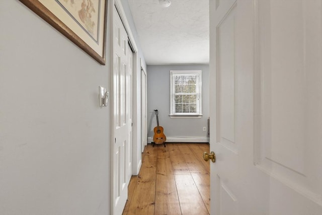 hallway featuring a baseboard heating unit, baseboards, and light wood finished floors