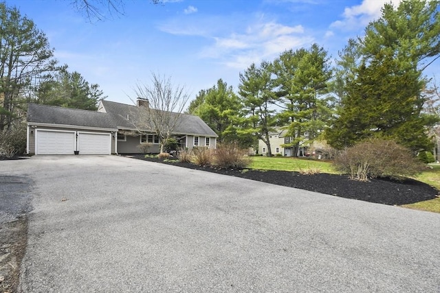 single story home featuring a chimney, an attached garage, and driveway