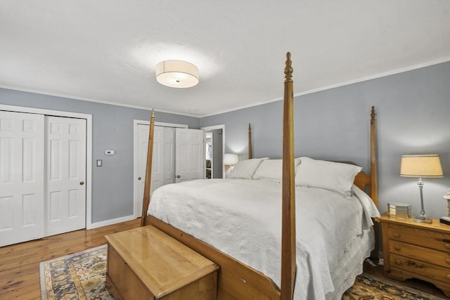 bedroom with two closets, crown molding, baseboards, and wood finished floors