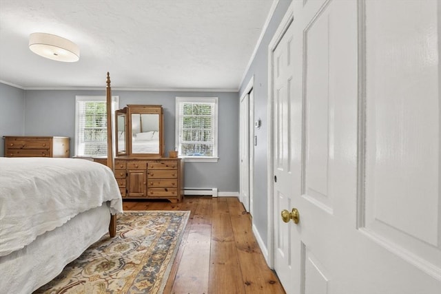 bedroom featuring crown molding, baseboard heating, multiple windows, and wood-type flooring