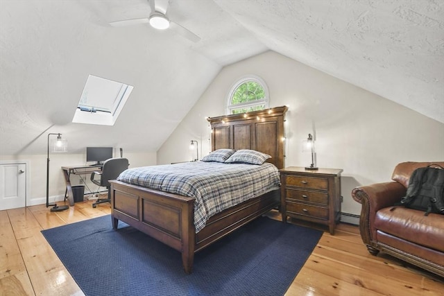 bedroom featuring a baseboard heating unit, ceiling fan, lofted ceiling with skylight, and light wood-style flooring