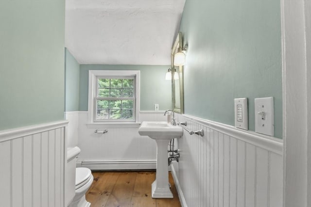 bathroom with a wainscoted wall, a sink, toilet, baseboard heating, and hardwood / wood-style floors