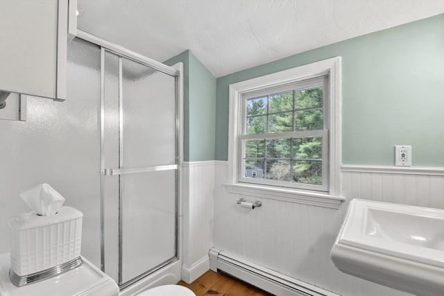 bathroom with a wainscoted wall, wood finished floors, a baseboard radiator, and a stall shower