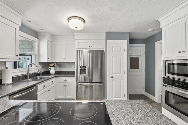 kitchen featuring appliances with stainless steel finishes, baseboards, white cabinetry, and a sink