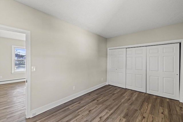 unfurnished bedroom featuring dark hardwood / wood-style flooring, baseboard heating, and a closet