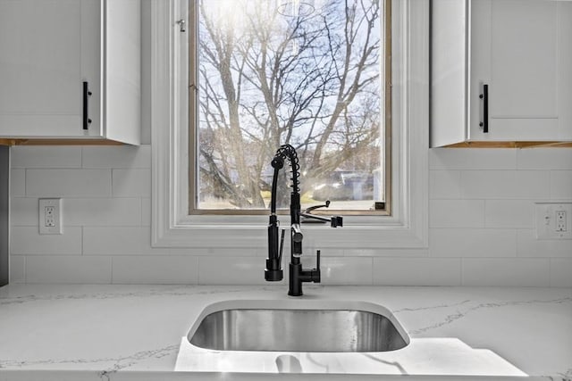 interior details featuring white cabinets, light stone counters, and sink