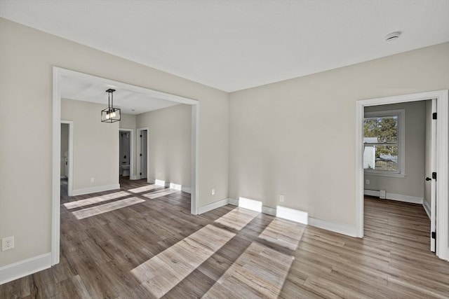 spare room featuring hardwood / wood-style floors, a baseboard radiator, and a notable chandelier