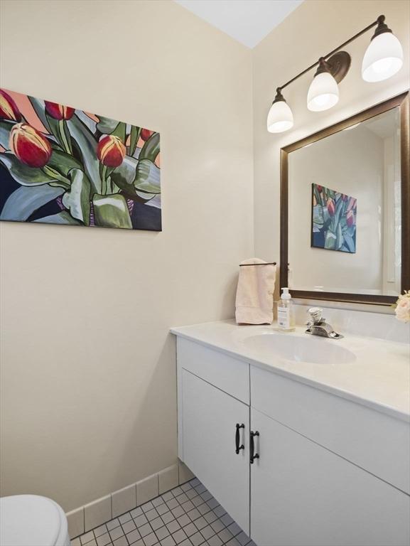 half bath with tile patterned flooring, toilet, vanity, and baseboards