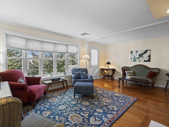 living room with crown molding, wood finished floors, visible vents, and baseboards