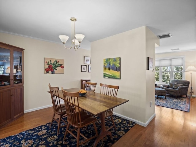 dining room with a notable chandelier, visible vents, baseboards, and hardwood / wood-style floors