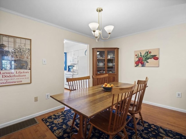 dining space with visible vents, a notable chandelier, ornamental molding, wood finished floors, and baseboards