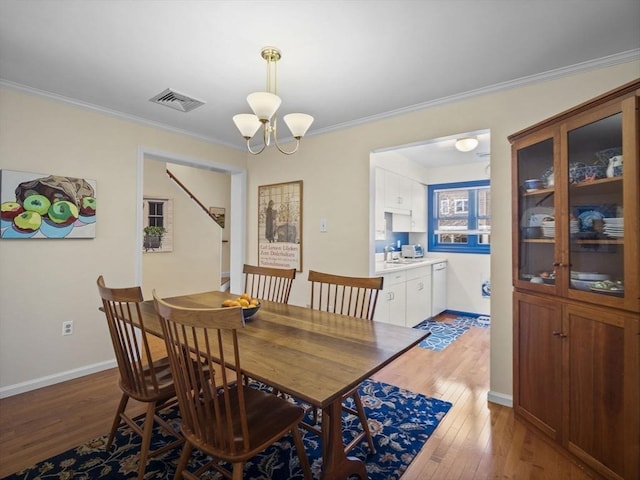 dining space with an inviting chandelier, visible vents, light wood finished floors, and ornamental molding