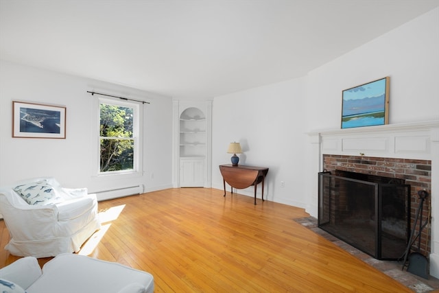 living room featuring a brick fireplace, built in features, light hardwood / wood-style floors, and a baseboard heating unit