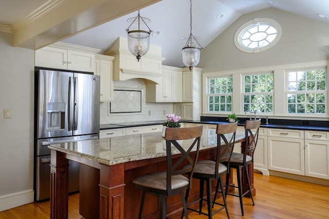 kitchen with light wood finished floors, stainless steel fridge, decorative backsplash, a breakfast bar area, and dark stone countertops