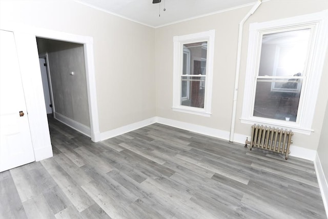 empty room with hardwood / wood-style flooring, ornamental molding, radiator heating unit, and ceiling fan