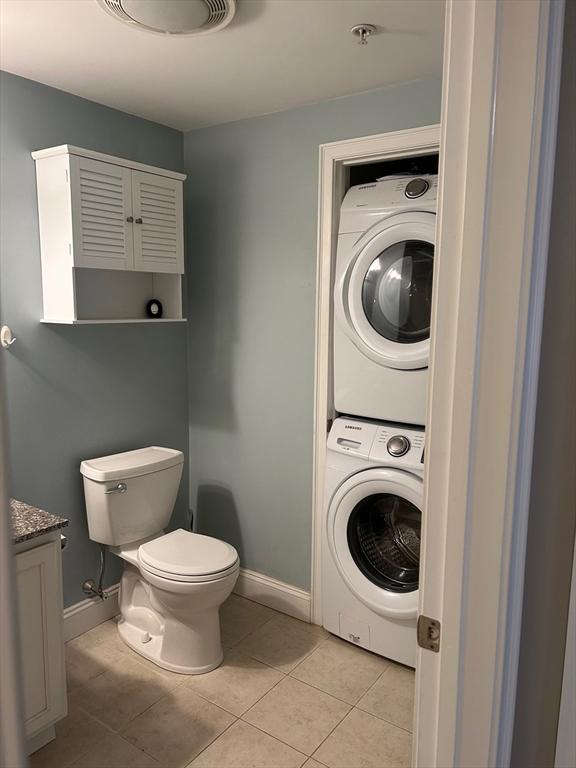 bathroom featuring tile patterned flooring, stacked washer and dryer, vanity, and toilet