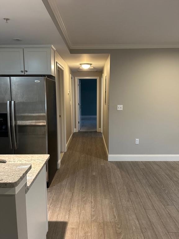 kitchen with stainless steel refrigerator with ice dispenser, white cabinetry, light stone counters, ornamental molding, and dark hardwood / wood-style flooring