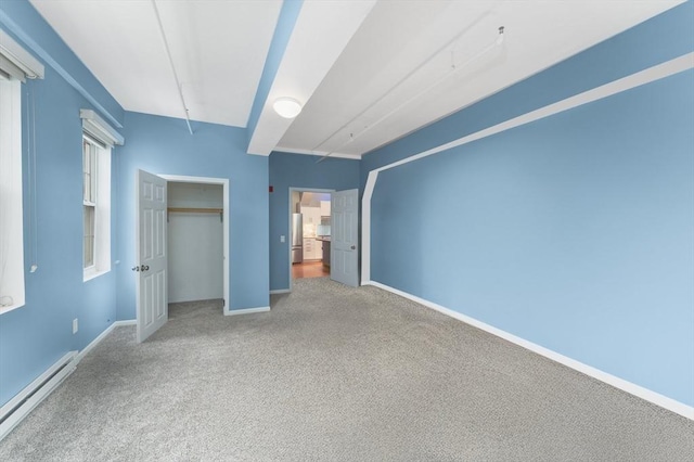 unfurnished bedroom featuring a closet, a baseboard heating unit, freestanding refrigerator, carpet flooring, and baseboards