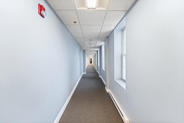 hallway with dark colored carpet, baseboards, a drop ceiling, and baseboard heating