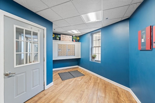 interior space featuring a paneled ceiling, wood finished floors, mail area, and baseboards