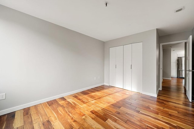 unfurnished bedroom with a closet, hardwood / wood-style flooring, and stainless steel refrigerator