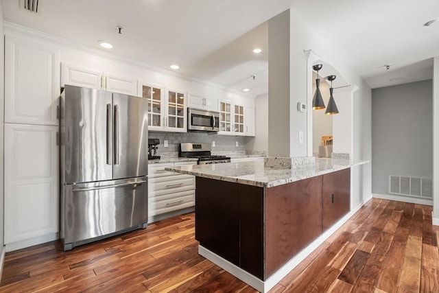 kitchen with appliances with stainless steel finishes, light stone counters, white cabinetry, dark wood-type flooring, and kitchen peninsula