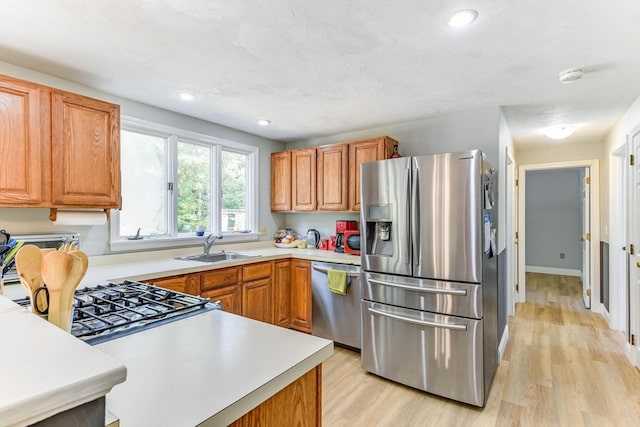 kitchen with appliances with stainless steel finishes, sink, and light hardwood / wood-style flooring