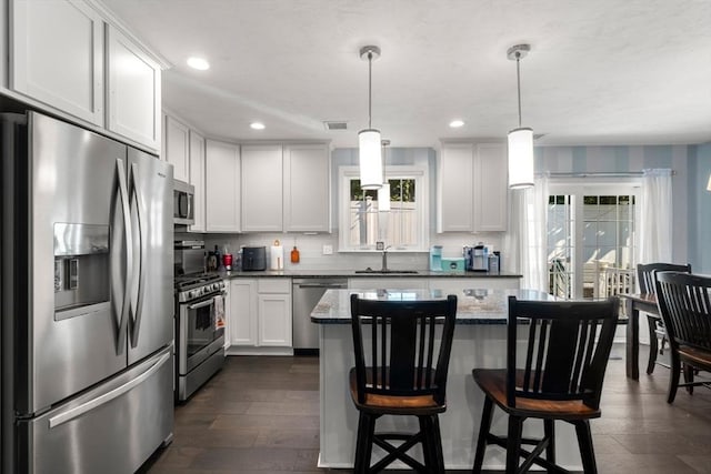 kitchen with stainless steel appliances, a center island, decorative light fixtures, white cabinets, and sink