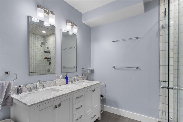 full bath featuring tiled shower, tile patterned flooring, double vanity, and baseboards