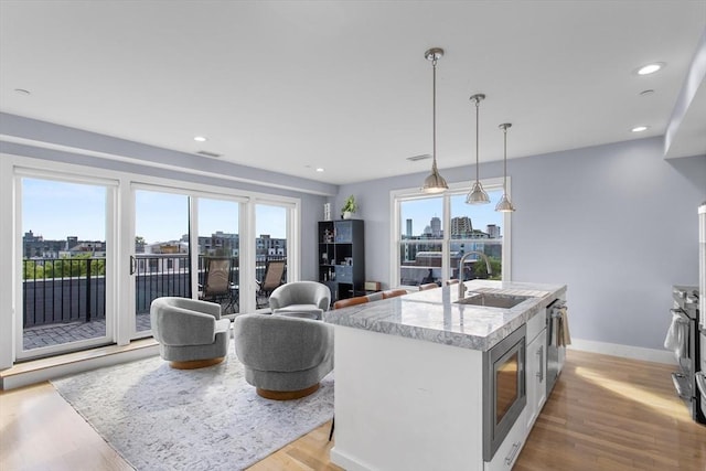 kitchen featuring a sink, stainless steel microwave, light wood-style flooring, a kitchen island with sink, and pendant lighting