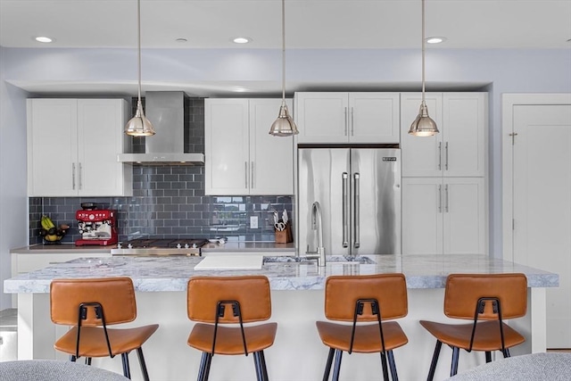 kitchen featuring wall chimney exhaust hood, high quality fridge, a sink, backsplash, and white cabinetry