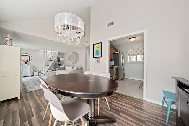 dining area with dark hardwood / wood-style floors, high vaulted ceiling, and a notable chandelier