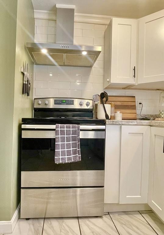 kitchen featuring white cabinets, decorative backsplash, wall chimney exhaust hood, marble finish floor, and stainless steel electric stove