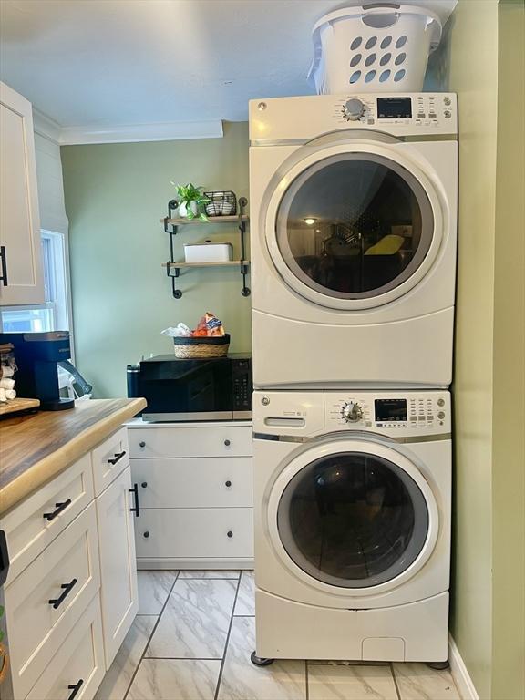 laundry room featuring marble finish floor, ornamental molding, and stacked washer and clothes dryer