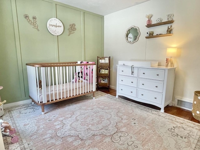 unfurnished bedroom featuring a crib, baseboards, visible vents, and wood finished floors