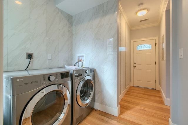 laundry room with ornamental molding, light hardwood / wood-style flooring, tile walls, and washing machine and clothes dryer