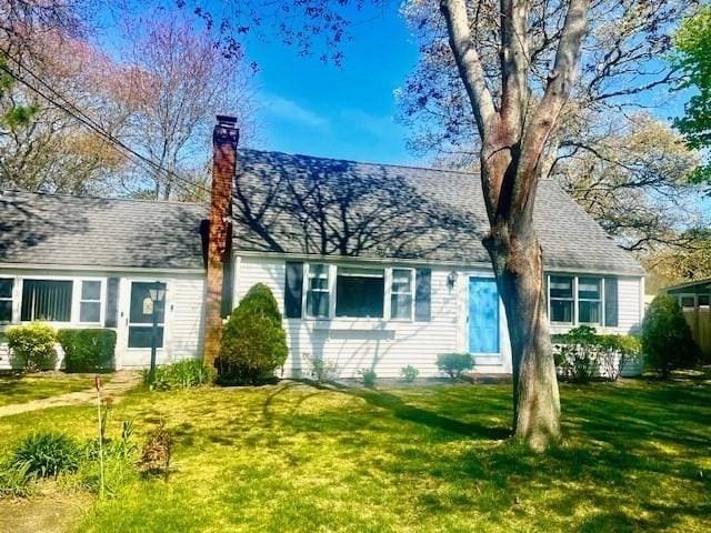 view of front of house featuring a front lawn, a chimney, and a shingled roof