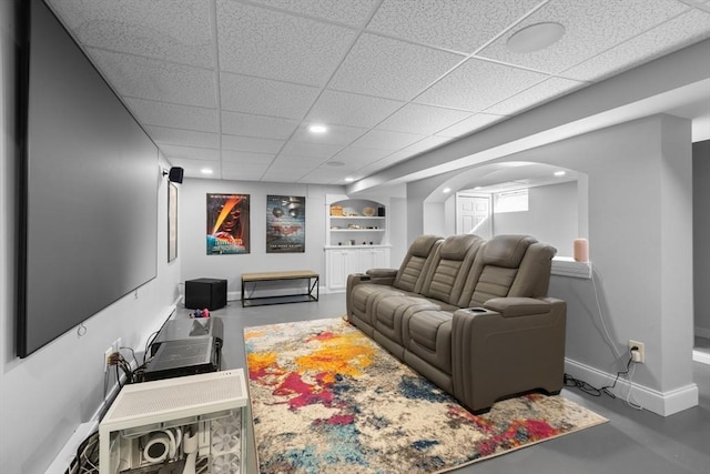 living room featuring a drop ceiling, finished concrete floors, recessed lighting, arched walkways, and baseboards