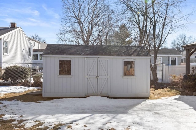 snow covered structure with an outbuilding, a shed, and fence