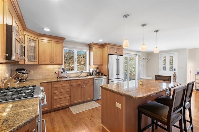 kitchen with a sink, a kitchen breakfast bar, light wood-style floors, appliances with stainless steel finishes, and light stone countertops