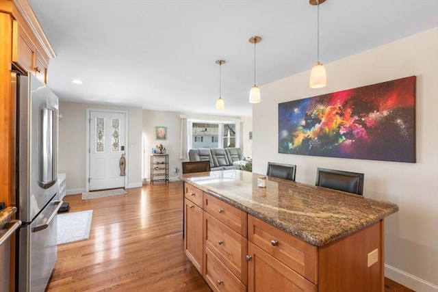 kitchen featuring dark stone countertops, light wood finished floors, a kitchen island, freestanding refrigerator, and decorative light fixtures