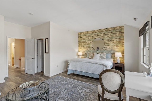 bedroom with visible vents, an accent wall, baseboards, vaulted ceiling, and wood finished floors