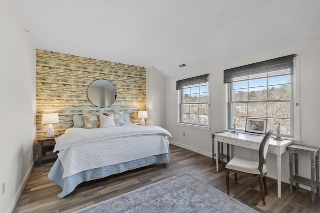 bedroom with visible vents, wood finished floors, baseboards, an accent wall, and vaulted ceiling