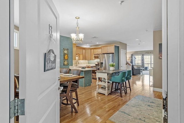 kitchen featuring a kitchen breakfast bar, light wood-type flooring, appliances with stainless steel finishes, and light brown cabinetry