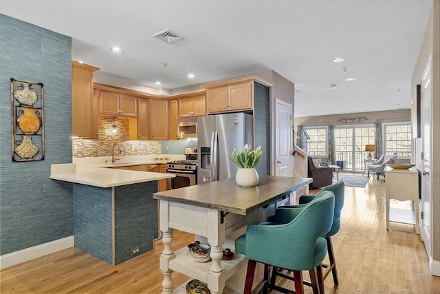 kitchen with visible vents, light wood-style flooring, appliances with stainless steel finishes, a peninsula, and a sink