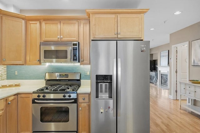 kitchen with stainless steel appliances, light wood finished floors, backsplash, and light countertops