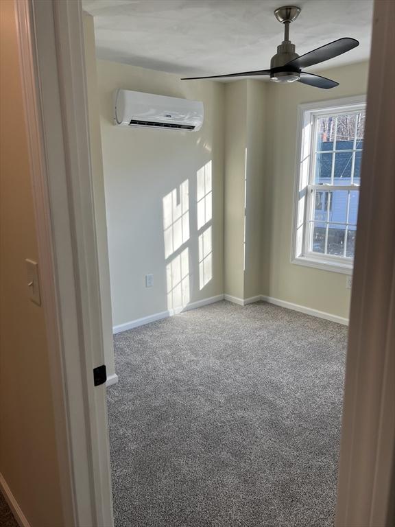 carpeted spare room with a wall unit AC and ceiling fan